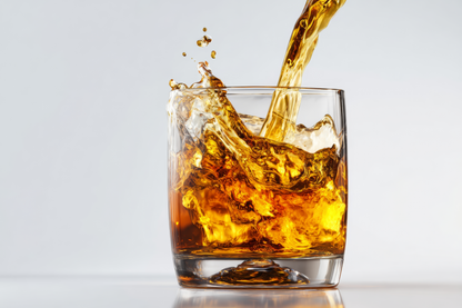 Goldfarbene Flüssigkeit wird in ein klares Glas gegossen und spritzt vor hellem Hintergrund auf