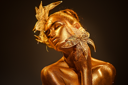 Künstlerisches Porträt einer Frau mit goldenem Glitzer-Make-up und floralen Schmuckelementen vor dunklem Hintergrund