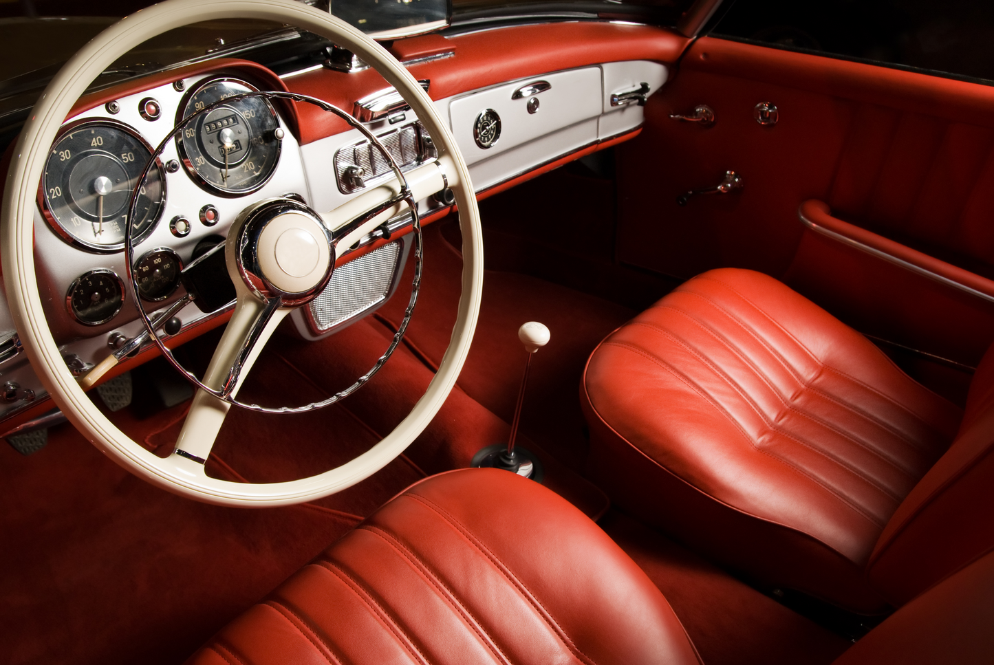 Detailansicht eines klassischen roten Autointerieurs mit Lenkrad, Armaturen und Ledersitzen