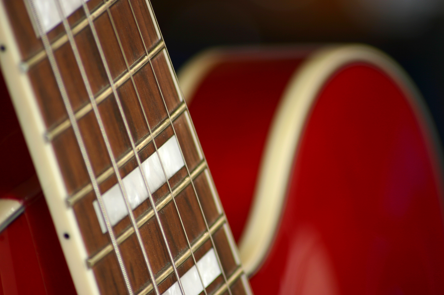 Nahaufnahme einer roten Gitarre mit sichtbarem Griffbrett, Saiten und unscharfem Gitarrenkörper im Hintergrund.