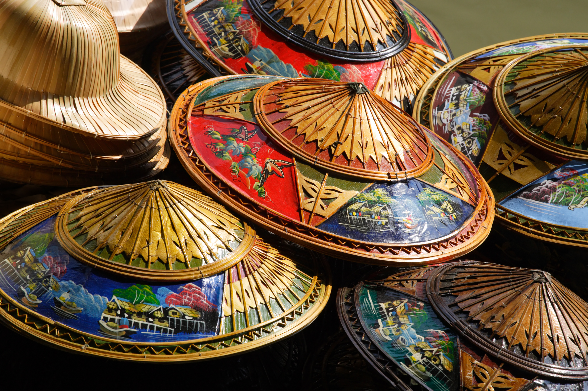 Nahaufnahme mehrerer bemalter asiatischer Bambushüte mit goldenen, roten und blauen Details als hochwertiges Kultur- und Objekt-Wandbild.
