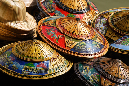 Nahaufnahme mehrerer bemalter asiatischer Bambushüte mit goldenen, roten und blauen Details als hochwertiges Kultur- und Objekt-Wandbild.