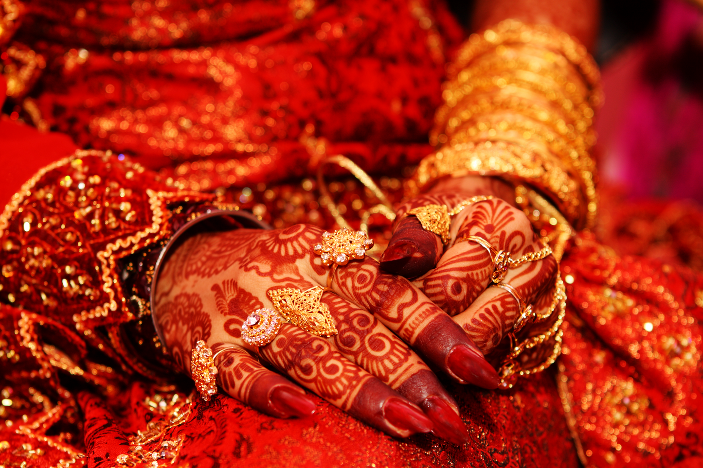 Nahaufnahme geschmückter Hände mit Henna-Mustern, goldenen Ringen und rotem Stoff als hochwertiges Kultur- und Detail-Wandbild.
