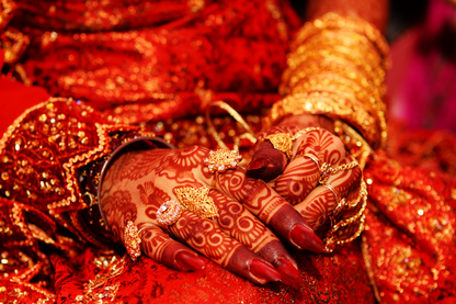 Nahaufnahme geschmückter Hände mit Henna-Mustern, goldenen Ringen und rotem Stoff als hochwertiges Kultur- und Detail-Wandbild.